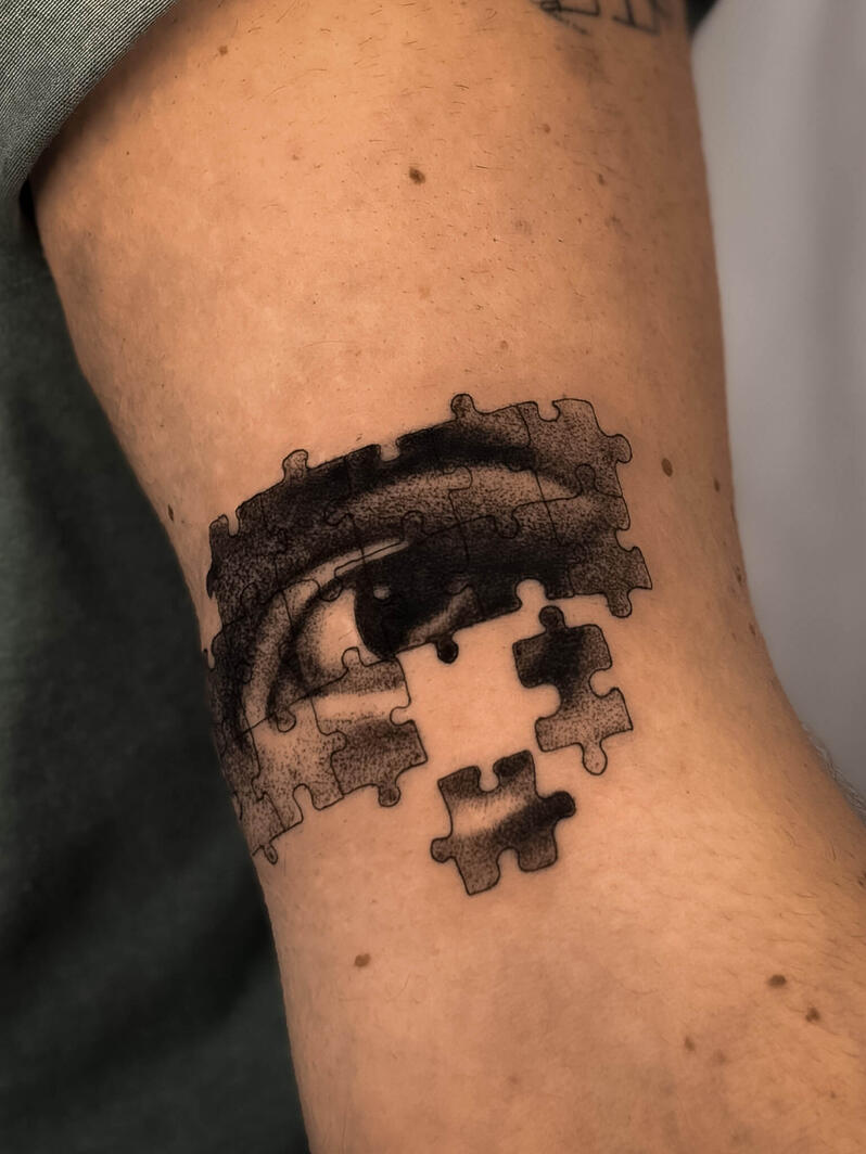 Tatuaggio realistico di un occhio integrato in un puzzle con pezzi mancanti sul braccio, in stile fine line e ombreggiature soft